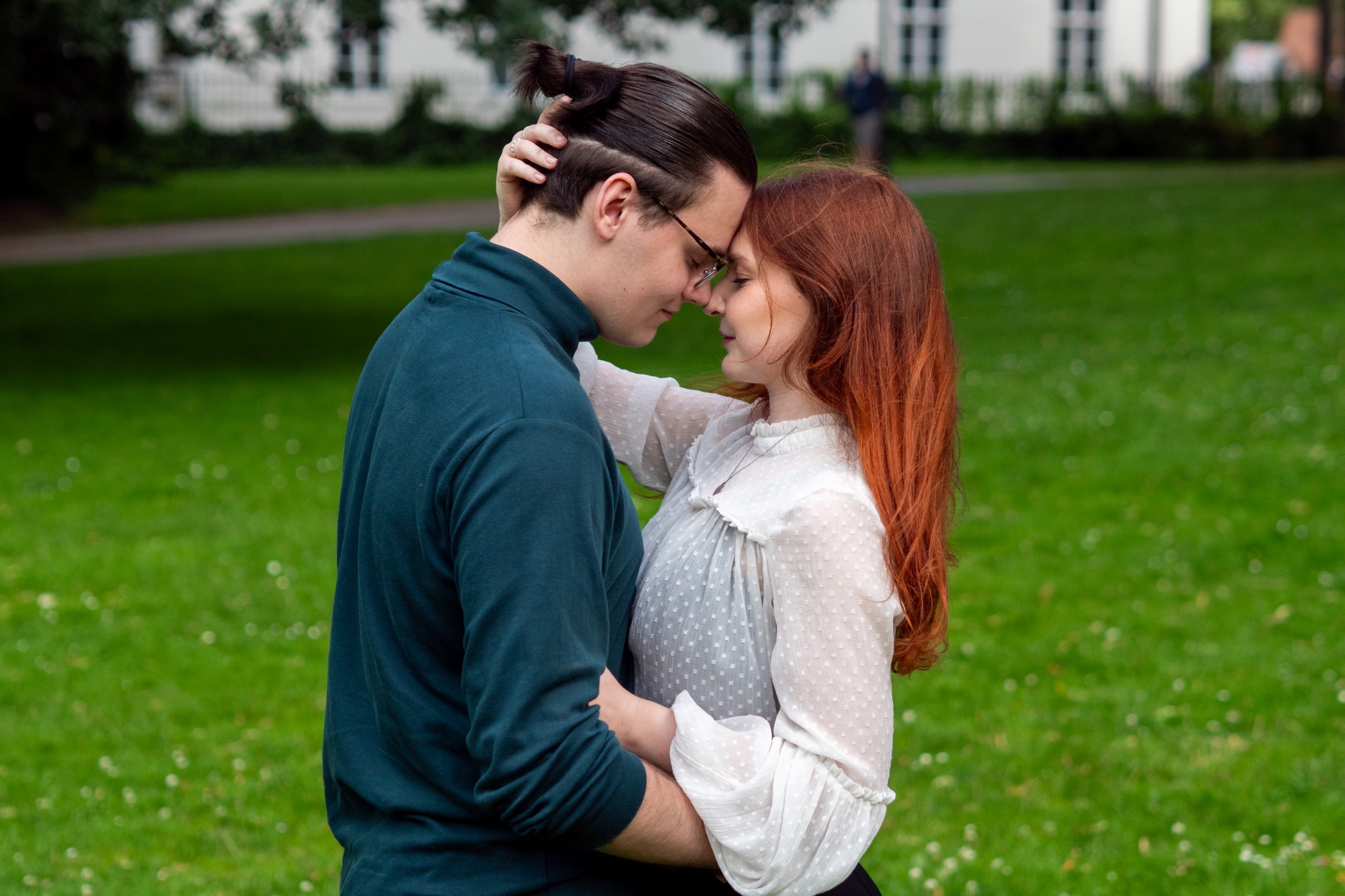 Couple holding each other closely on a green lawn.